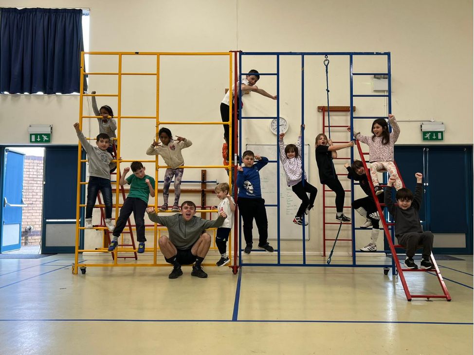 A Challenge coach with a class of children on climbing equipment in the school hall